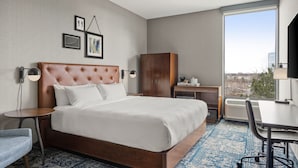 A hotel room with a large bed, a desk, a chair, a wardrobe, and a view of the city through a large window. - Four Points by Sheraton Chicago Westchester/Oak Brook (Westchester)