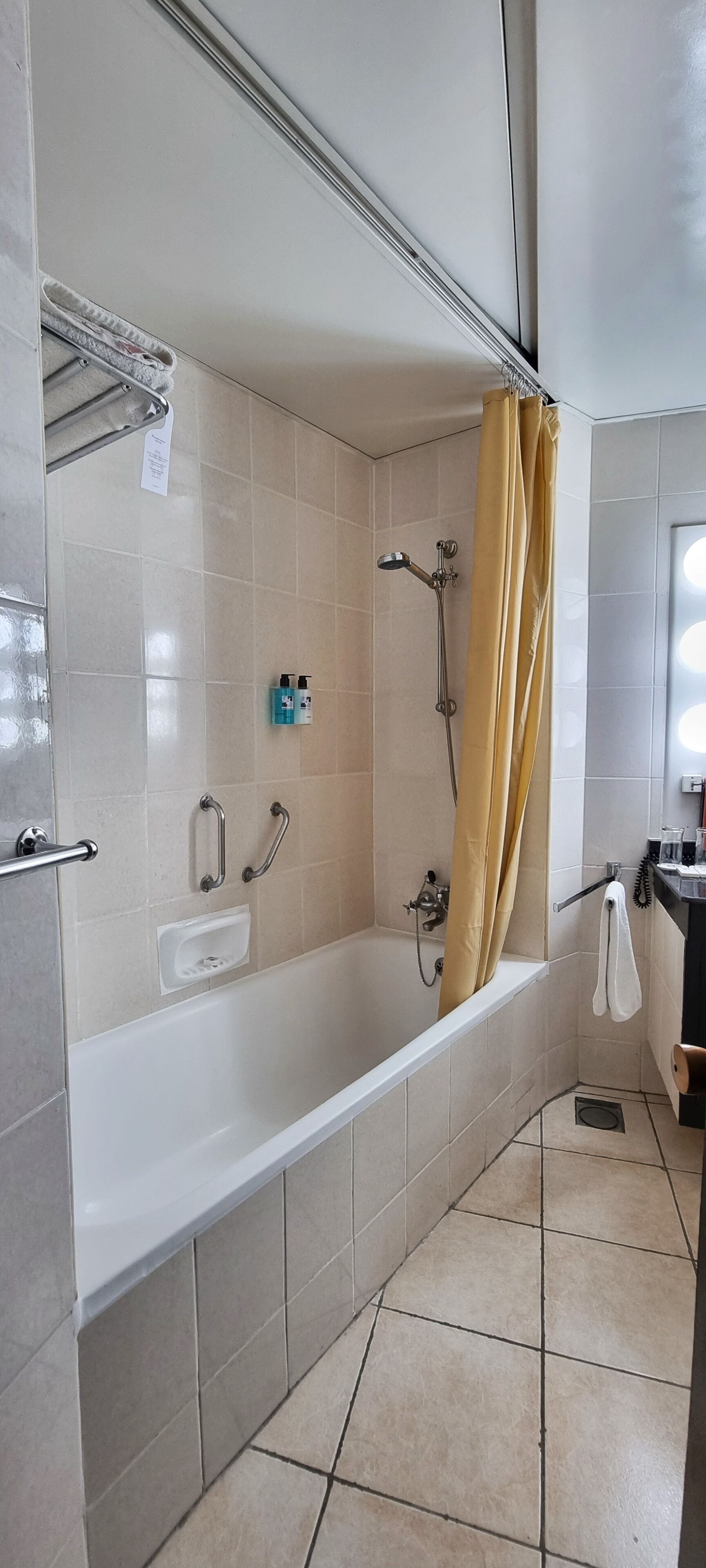 A bathroom with a bathtub, a shower, and a toilet. There are grab bars and a soap dispenser on the wall.