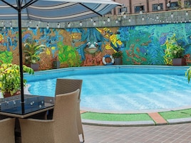 Zona de piscina con un mural colorido, sillas de mimbre y una mesa con futbolín.