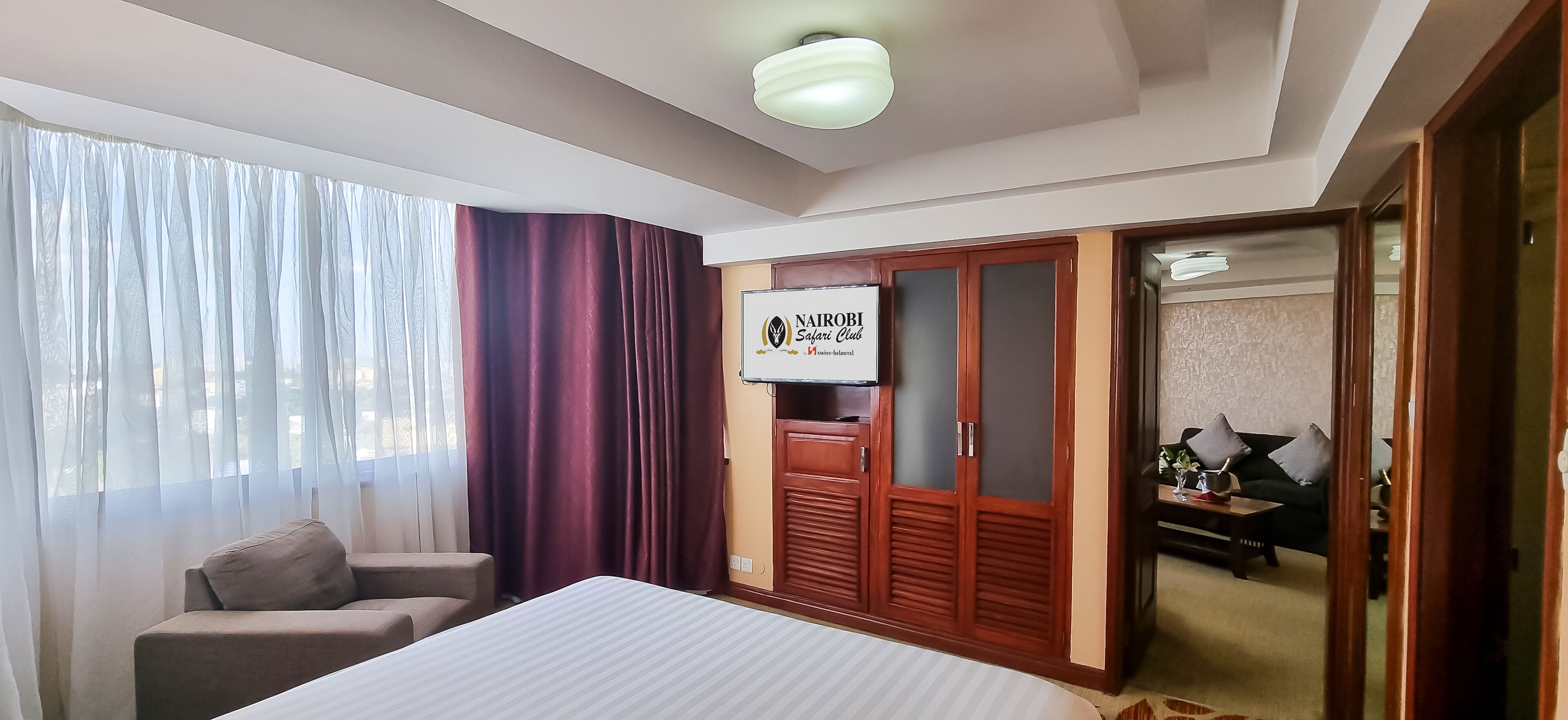 A hotel room with a bed, a desk, a chair, a wardrobe, and a mirror.