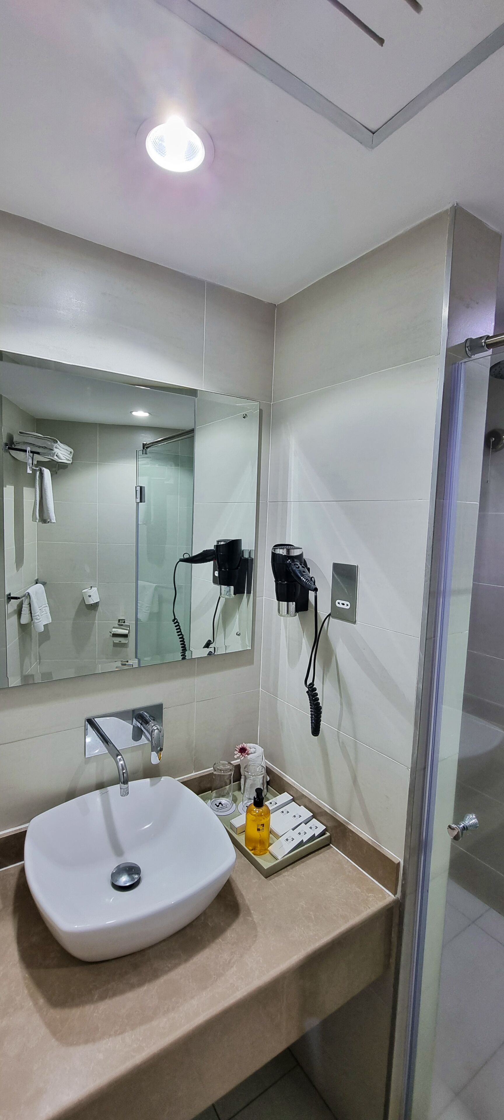 A modern bathroom with a large mirror, a sink, a hairdryer, and a shower.