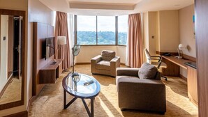 A modern hotel room with a large window, a flat-screen TV, a sofa, a desk, and a fan. - Nairobi Safari Club by Swiss-Belhotel (Nairobi)