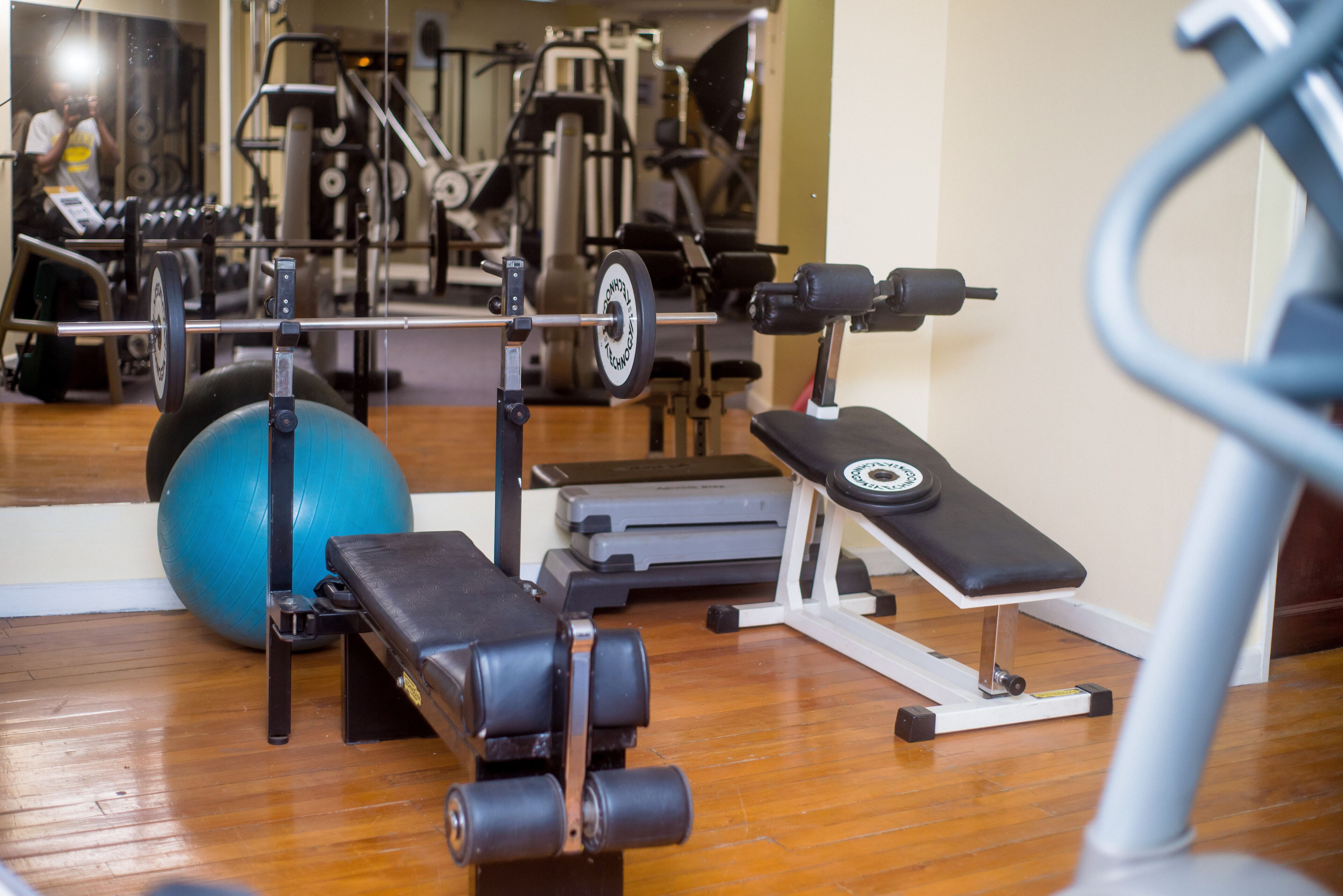 A gym with exercise equipment, a blue exercise ball, and a mirror reflecting the equipment.