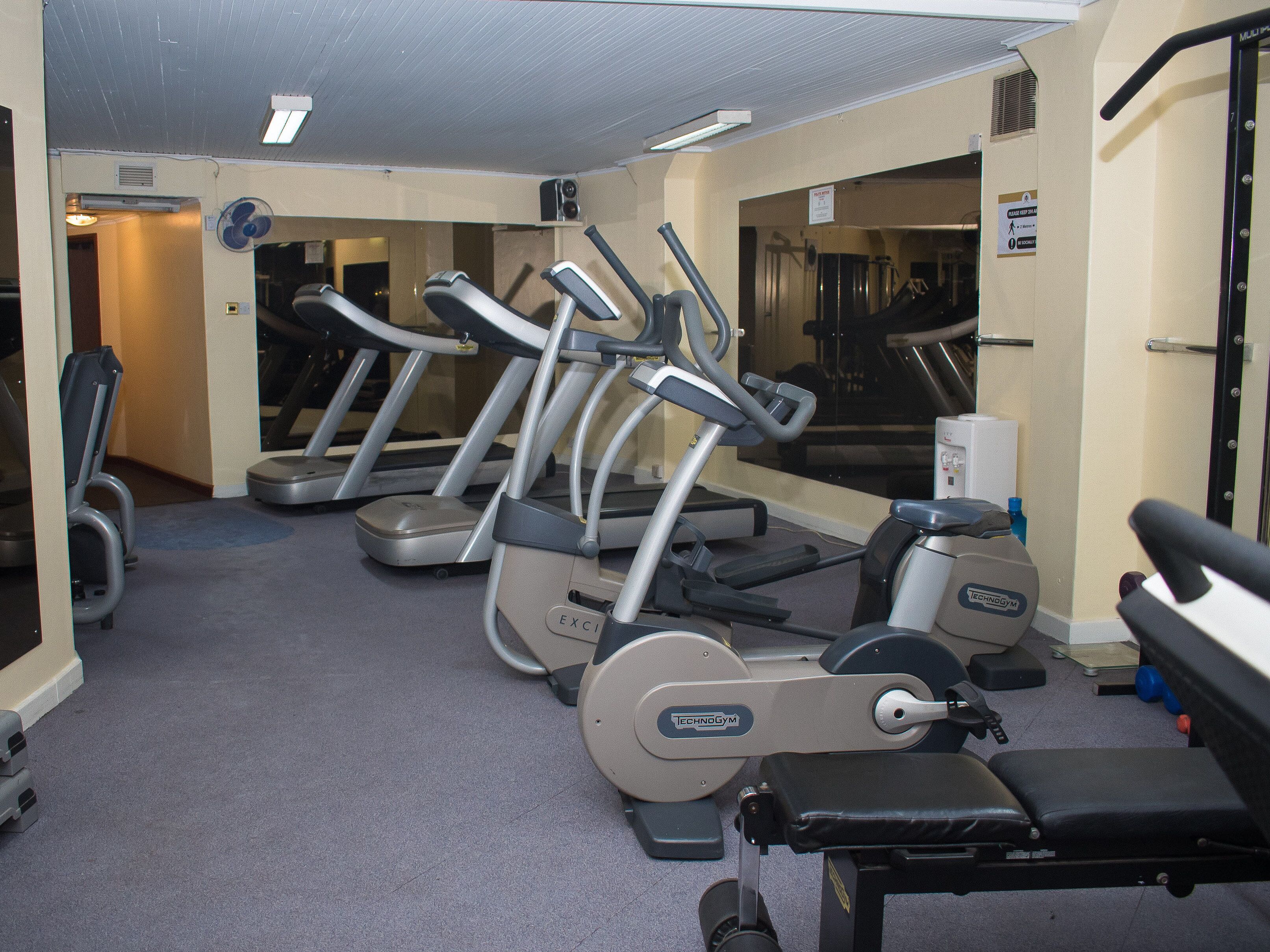 Un gimnasio con cintas de correr, una banca y una barra de pesas.
