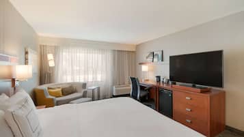 A hotel room with a large bed, a desk with a television, a sofa, and a window with curtains.