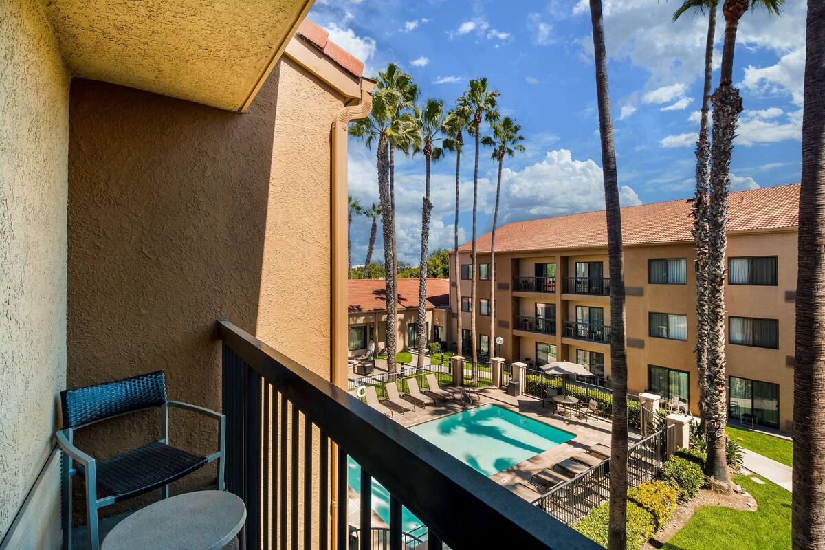 A balcony with a pool view, palm trees, and a building with multiple balconies.