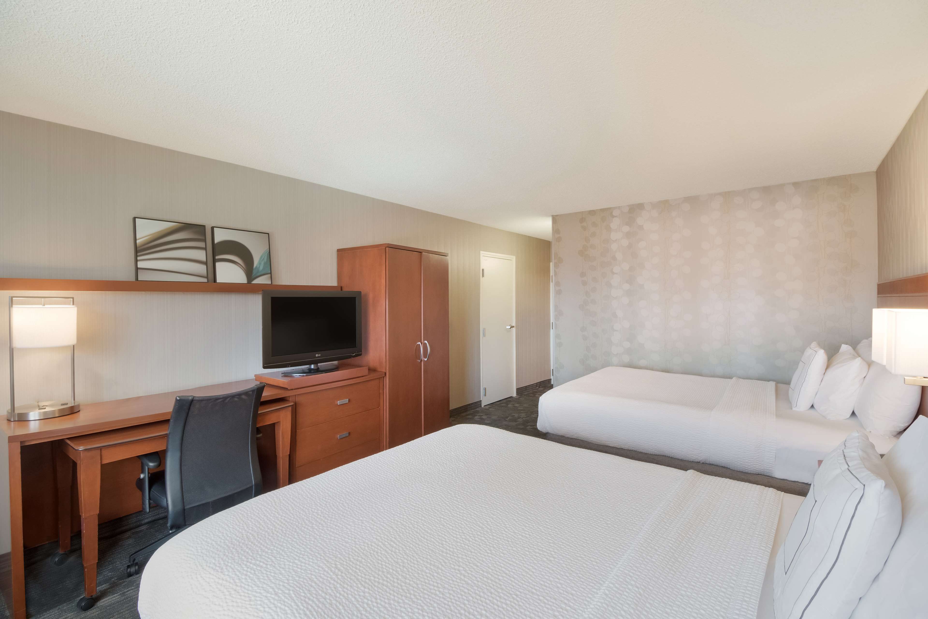 A hotel room with a large bed, a desk with a computer, a television, and a wardrobe.