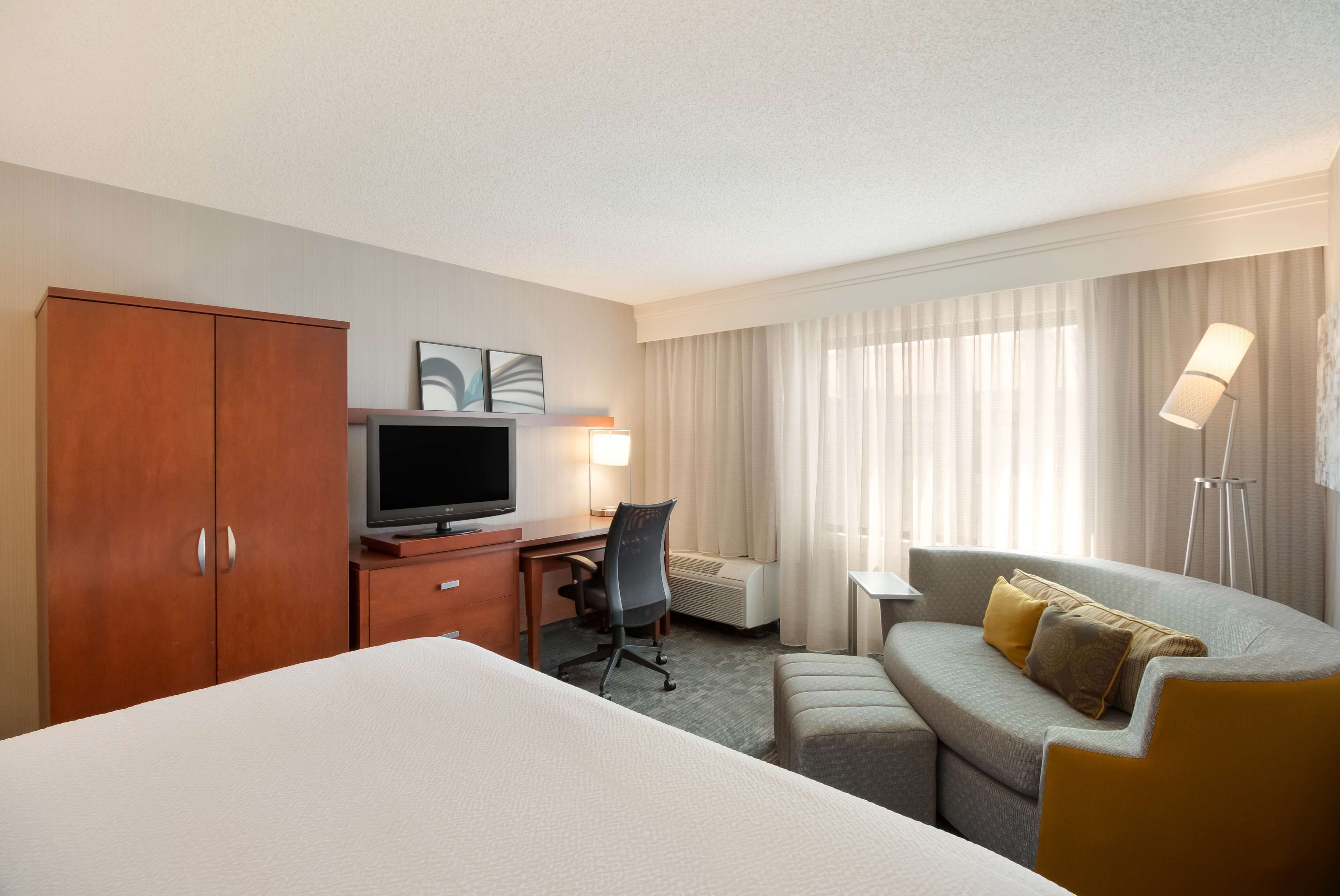 A hotel room with a bed, a desk with a computer, a sofa, and a TV.