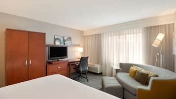 A hotel room with a bed, a desk with a computer, a sofa, and a TV.