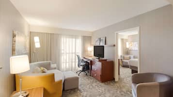 Quarto de hotel com sofá, escrivaninha com televisão, cadeira e abajur.