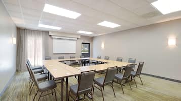 A conference room with a long table, chairs, a projector screen, and a whiteboard.