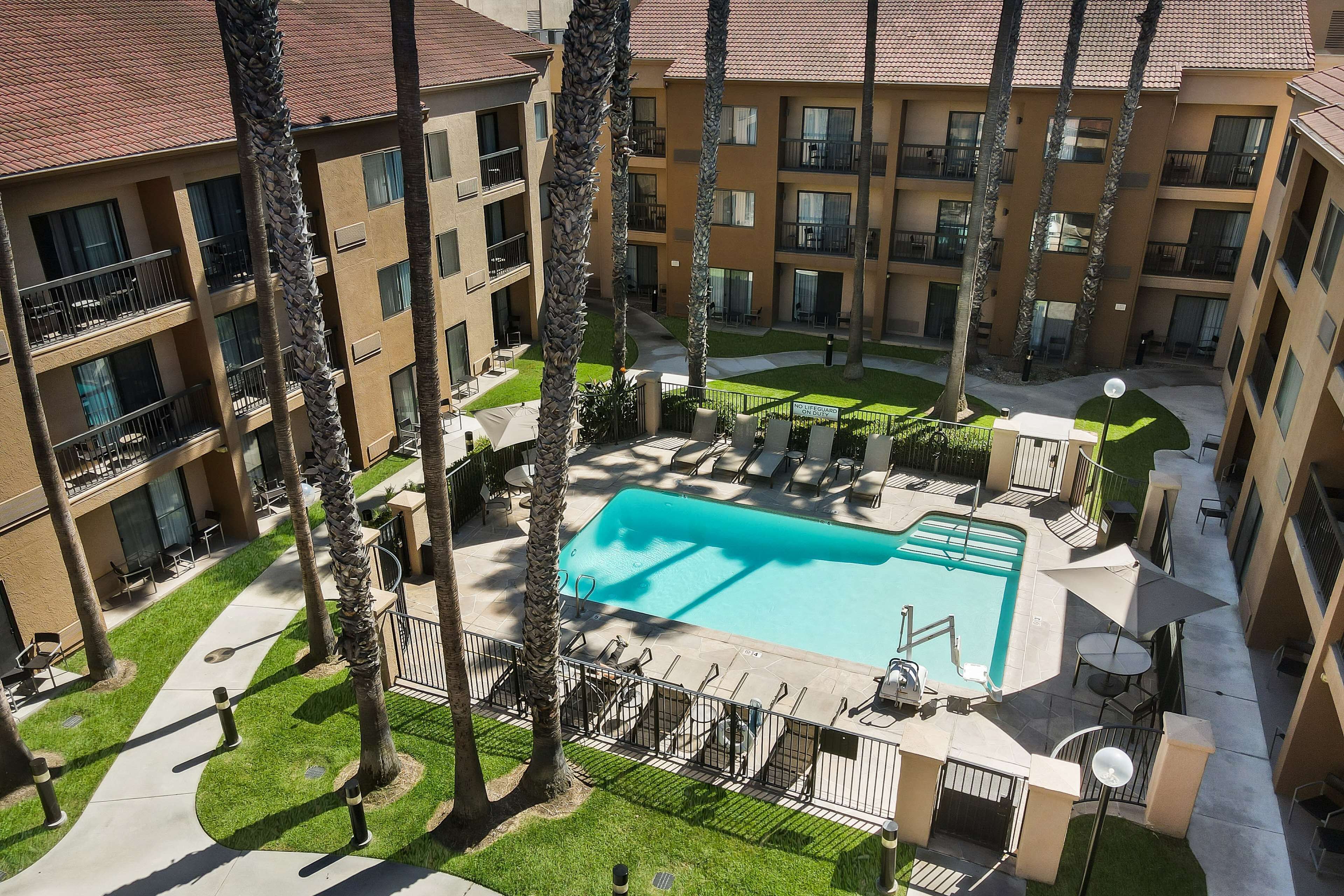 A multi-story hotel with a swimming pool surrounded by palm trees and outdoor seating.