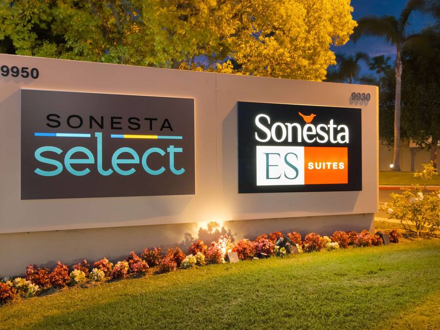 Un letrero de hotel con los logotipos 'SONESTA select' y 'Sonesta ES Suites', rodeado de un parterre floral.