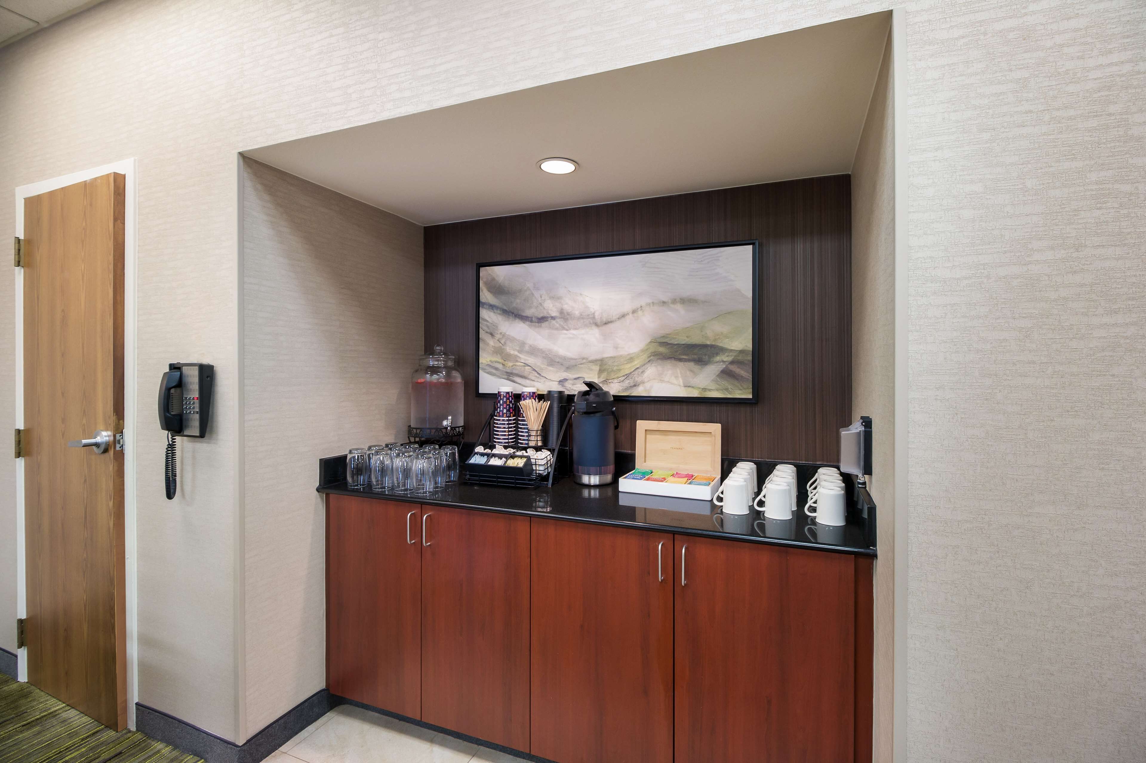 A hotel reception area with a wooden door, a phone, a coffee station, and a large abstract painting on the wall.