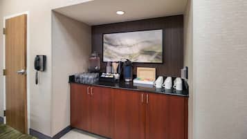 A hotel reception area with a wooden door, a phone, a coffee station, and a large abstract painting on the wall.