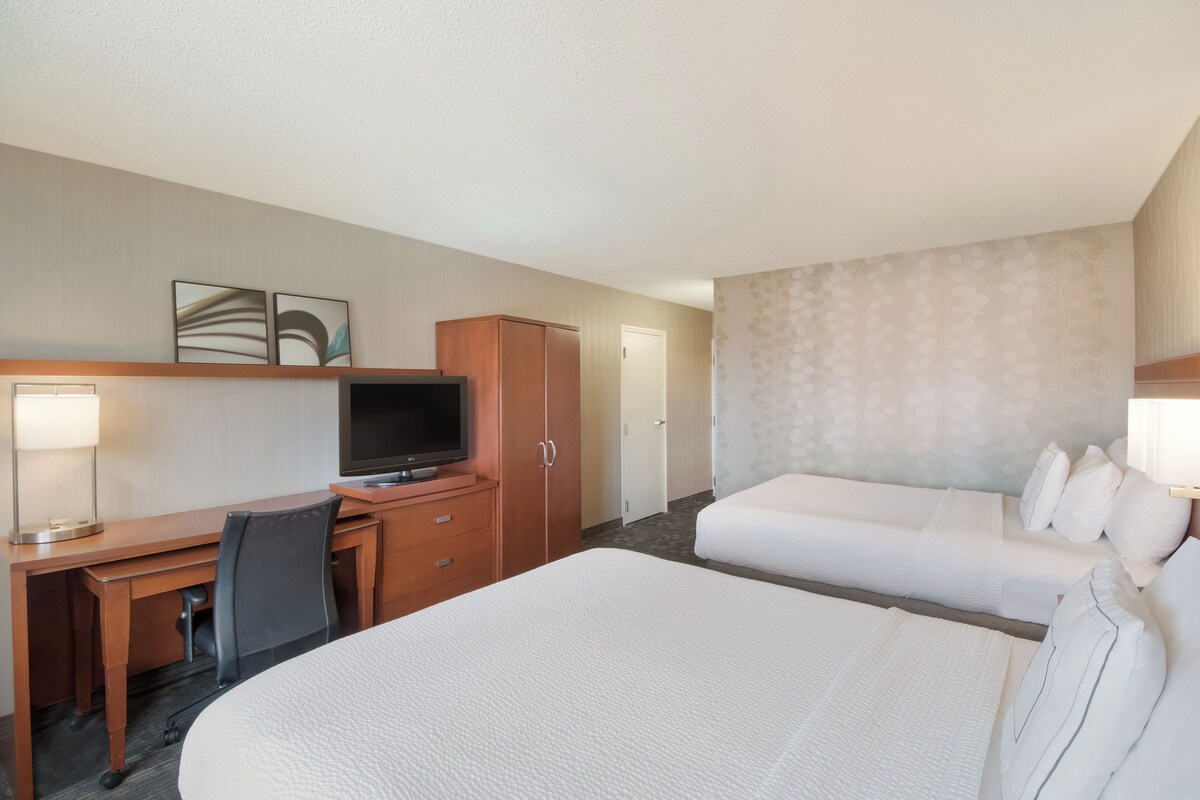 A hotel room with a large bed, a desk with a television, and a wardrobe.
