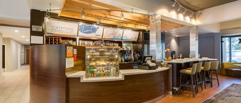 A modern bar area with a curved counter, a glass display case with snacks, and a seating area with bar stools.