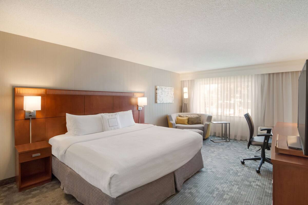 A hotel room with a large bed, a desk, a chair, a small table, and a TV.