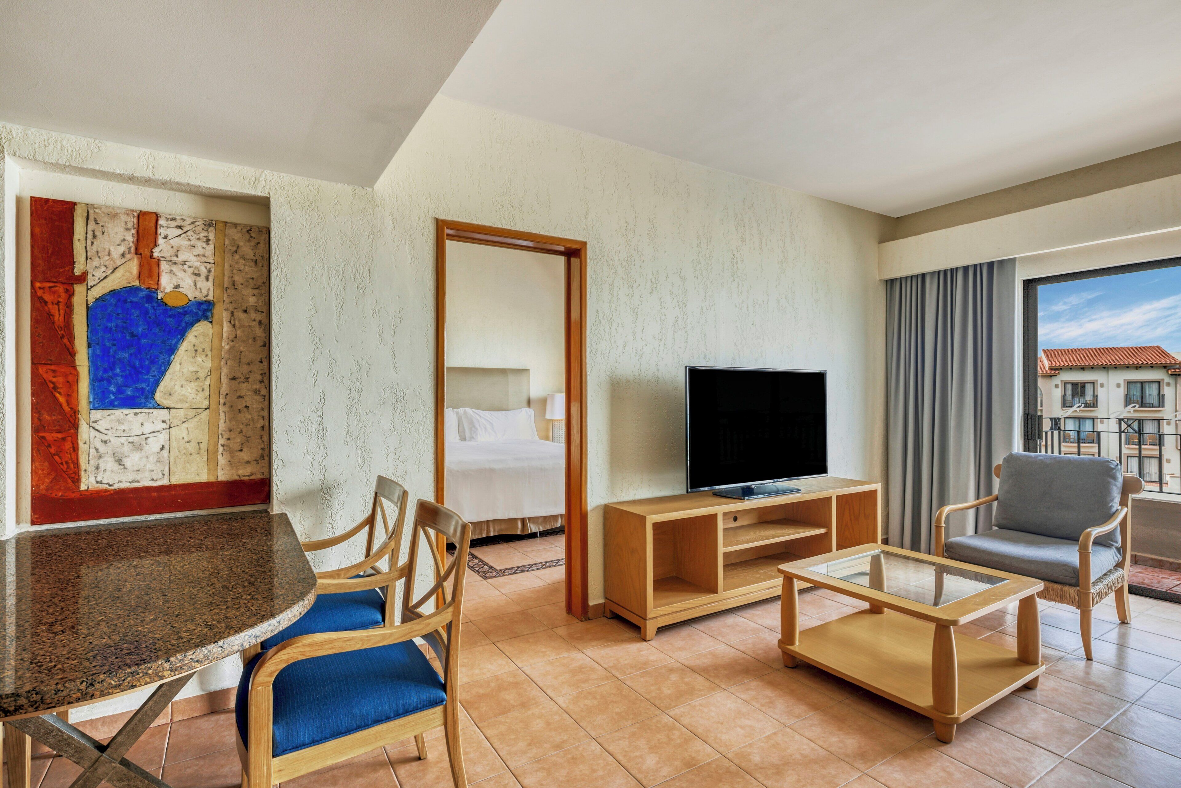 Ein Hotelzimmer mit Bett, Fernseher, Esstisch und einer Couch.