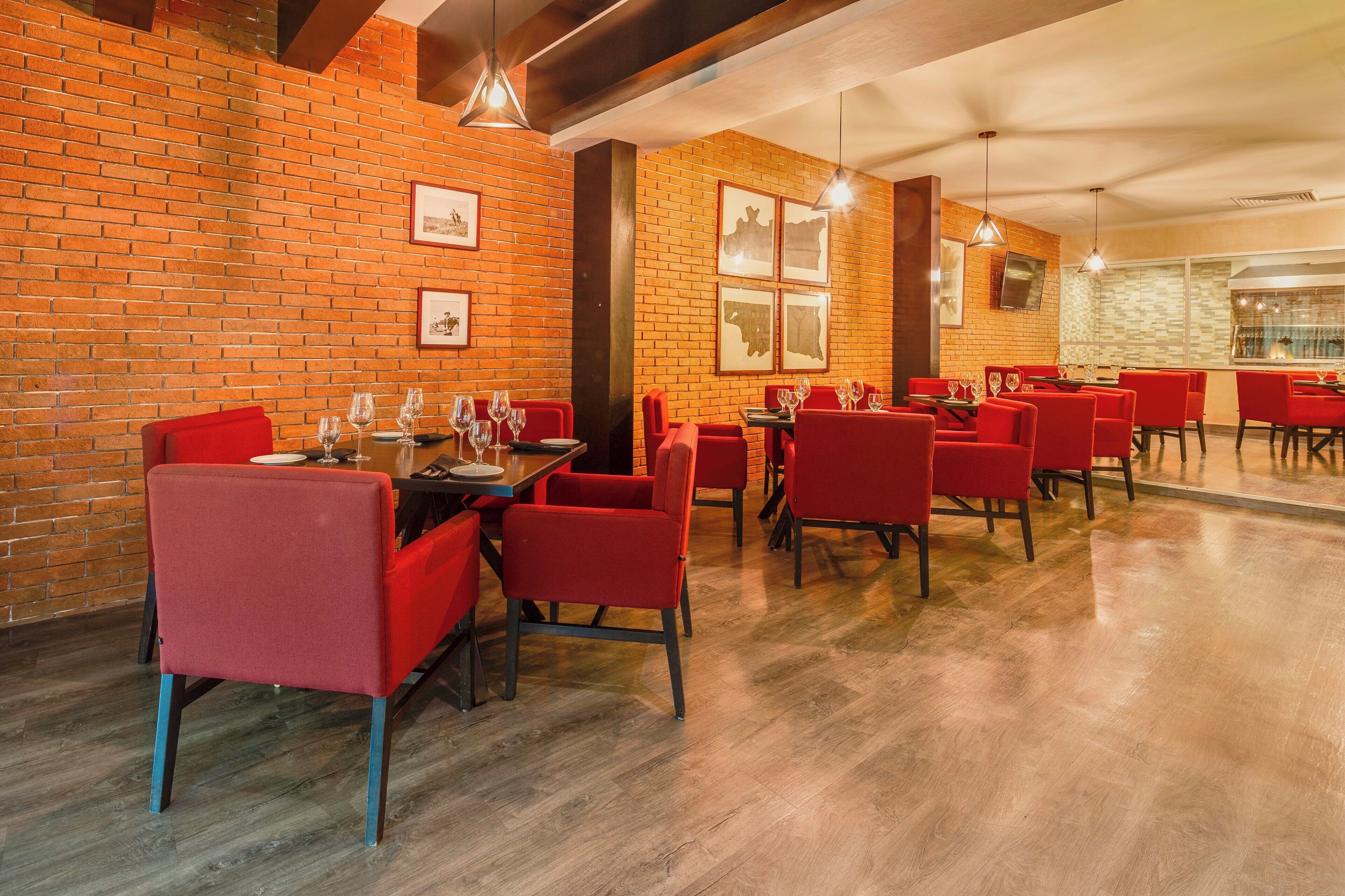 A restaurant with brick walls, red chairs, and wooden tables.