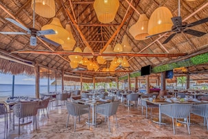 Un restaurante con techos de paja, varias mesas de comedor, sillas, ventiladores de techo y luces colgantes.
