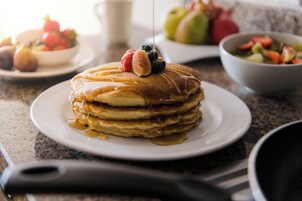 A stack of pancakes with fruit on top, syrup, and a knife on a plate.