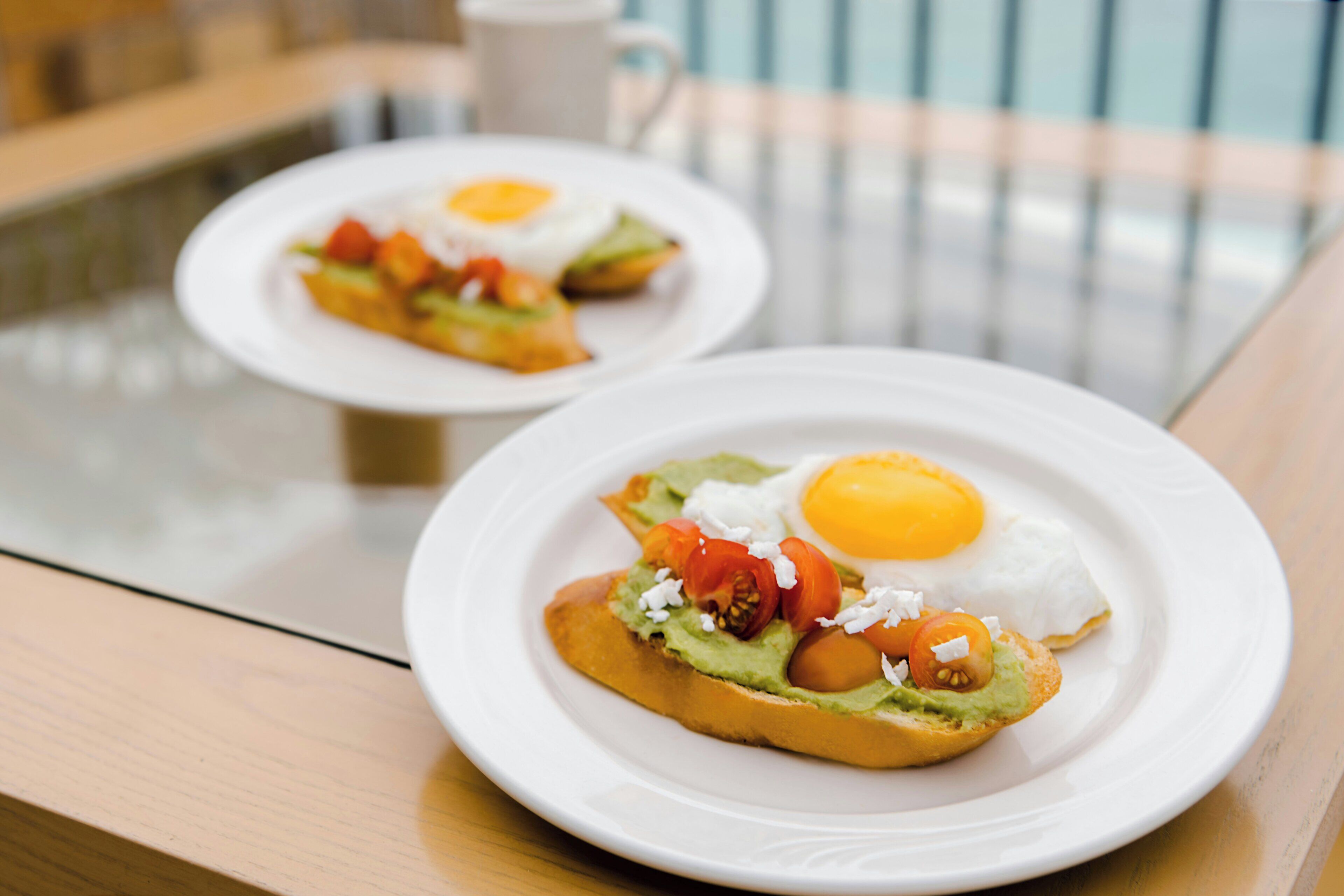 Dos platos de desayuno con huevos y aguacate sobre tostadas, sobre una mesa de madera.