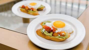 Dos platos de desayuno con huevos y aguacate sobre tostadas, sobre una mesa de madera.