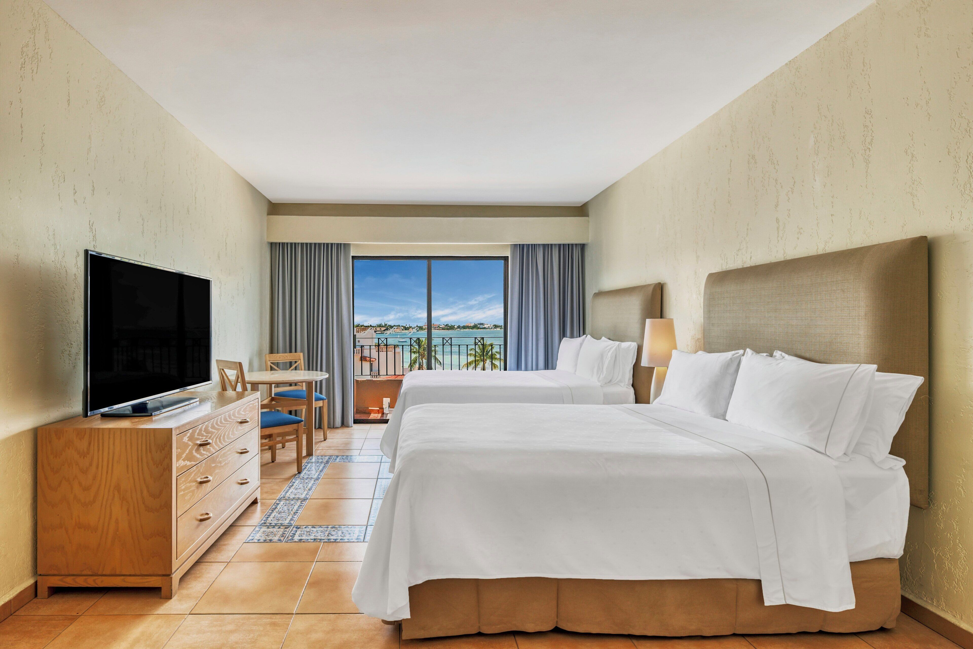 Een hotelkamer met een bed, een televisie, een bureau en uitzicht op zee.