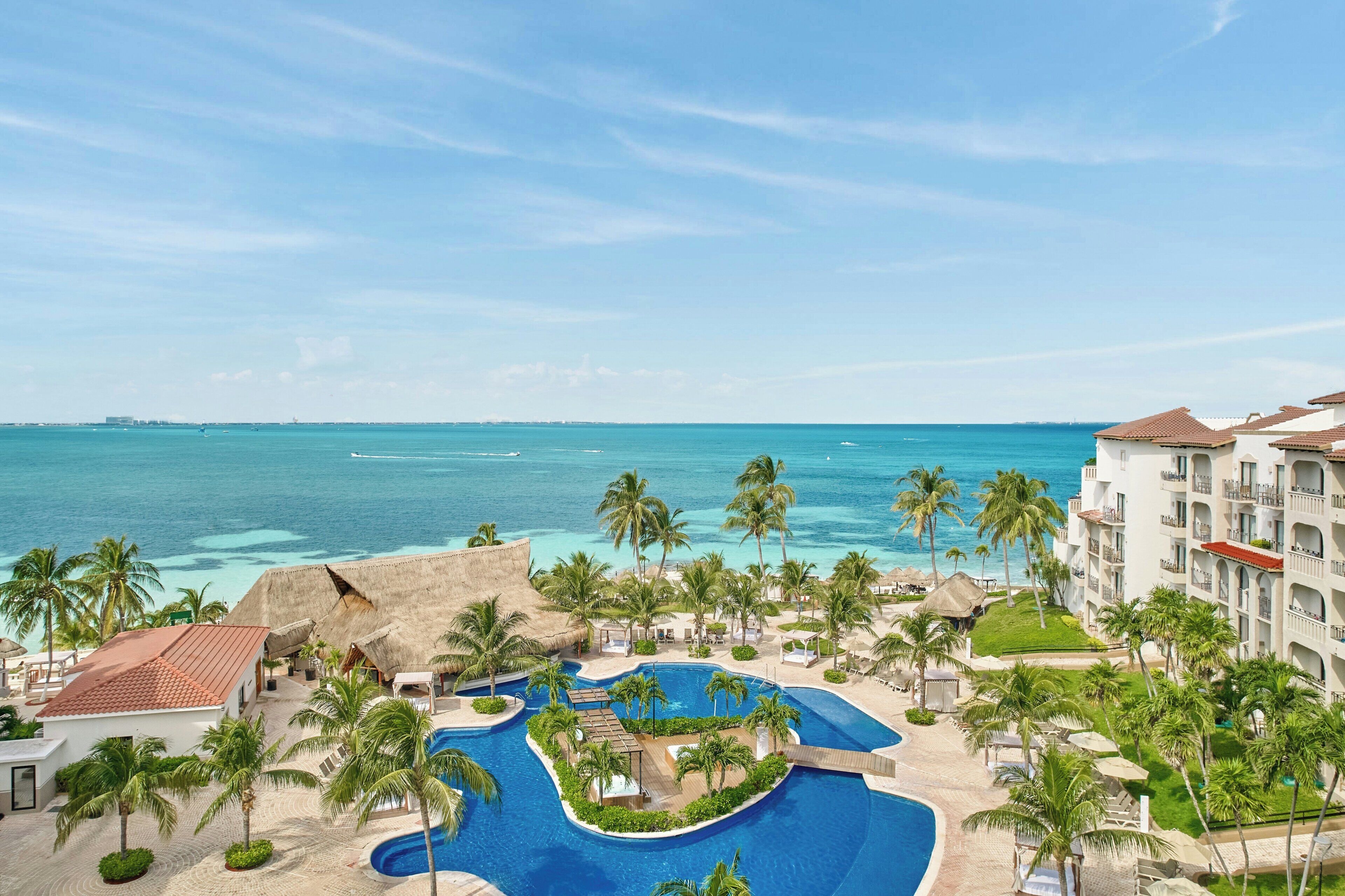 Um resort com piscina, palmeiras e vista para o oceano.