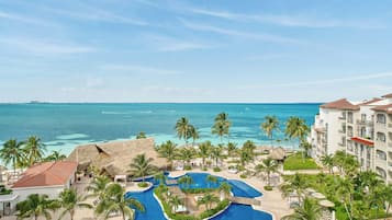 Um resort com piscina, palmeiras e vista para o oceano.