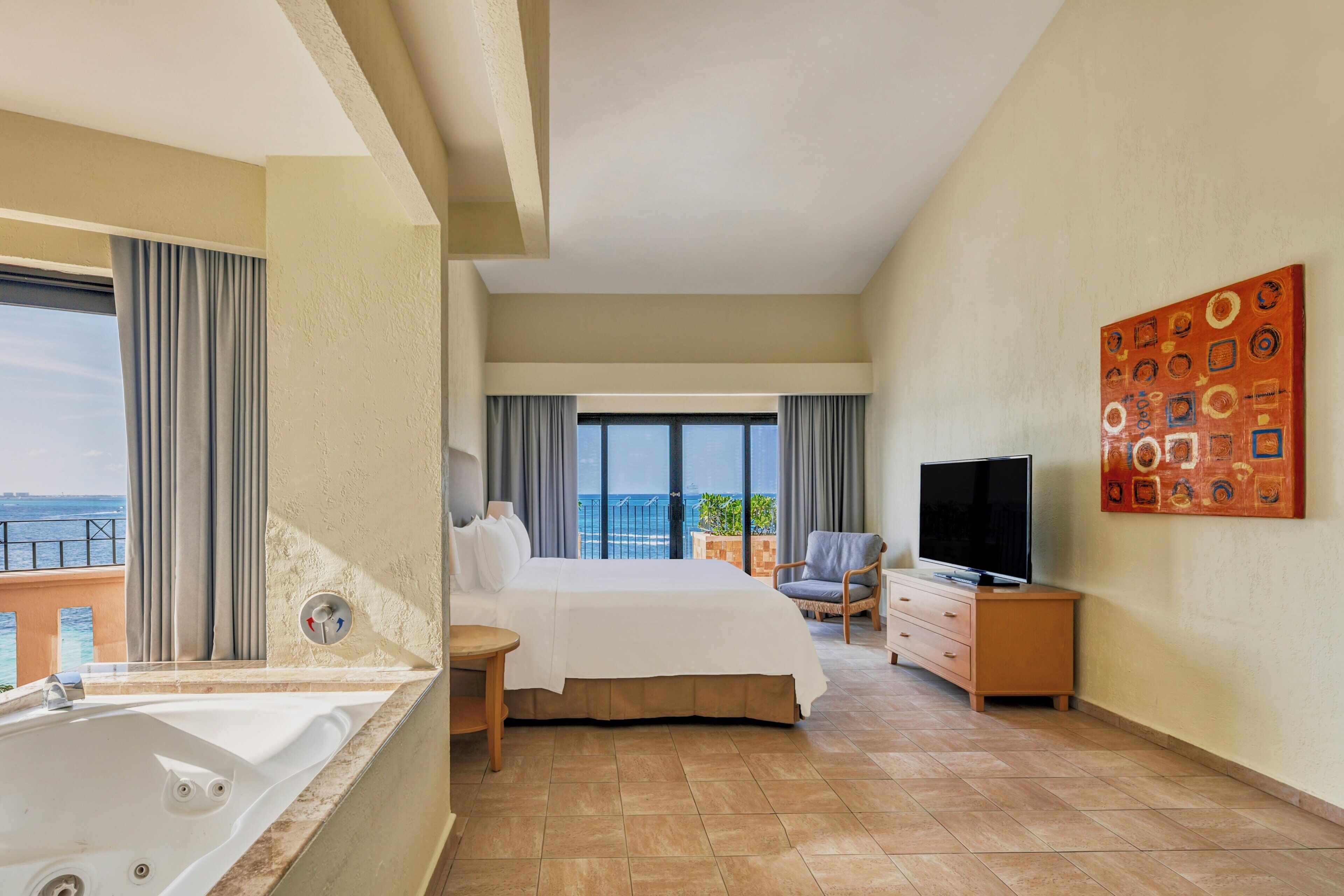 Habitación de hotel con una cama grande, televisión, una silla, un escritorio y vista al océano.