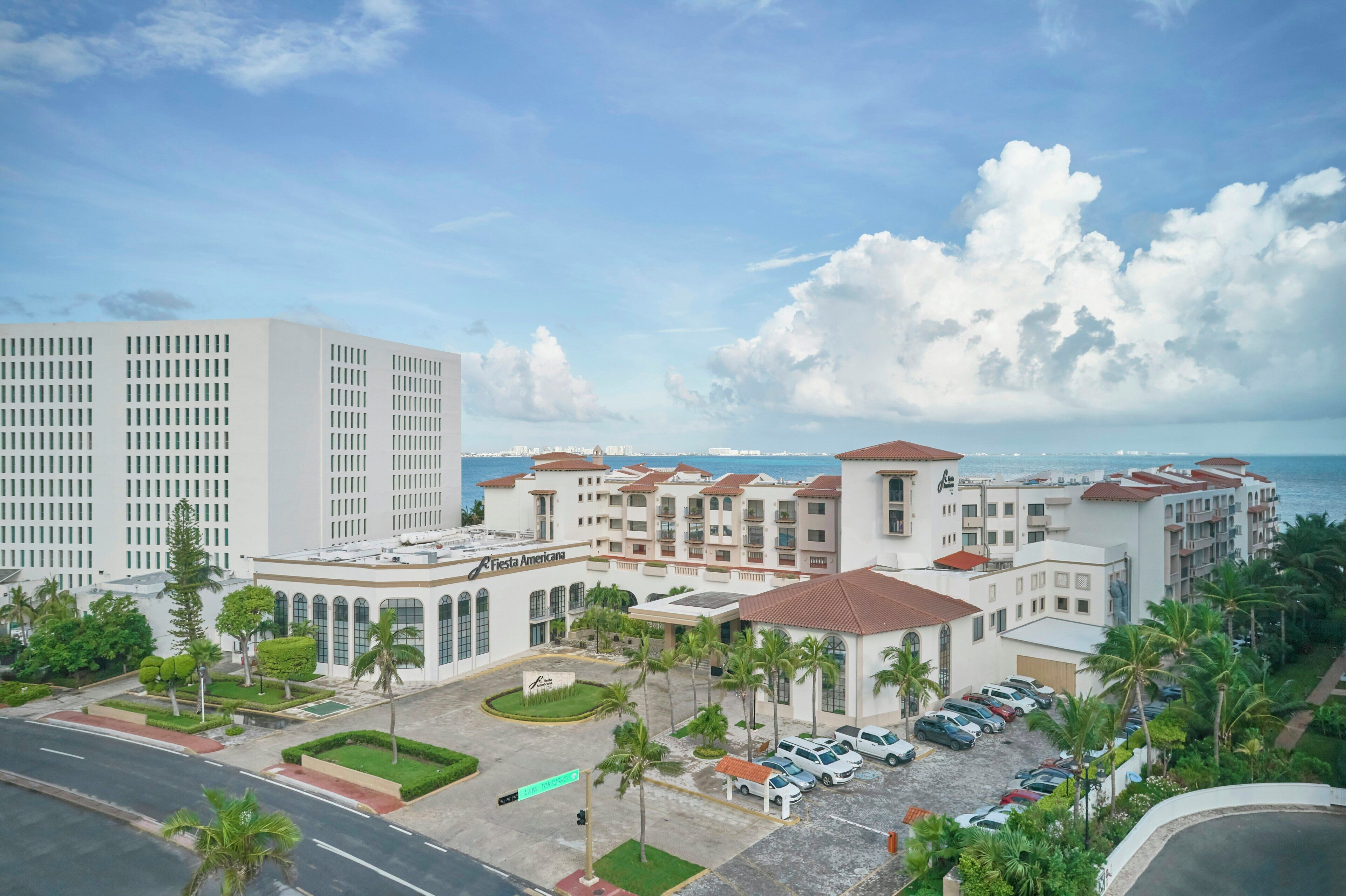 A hotel with a parking lot, a road, and a view of the sea.