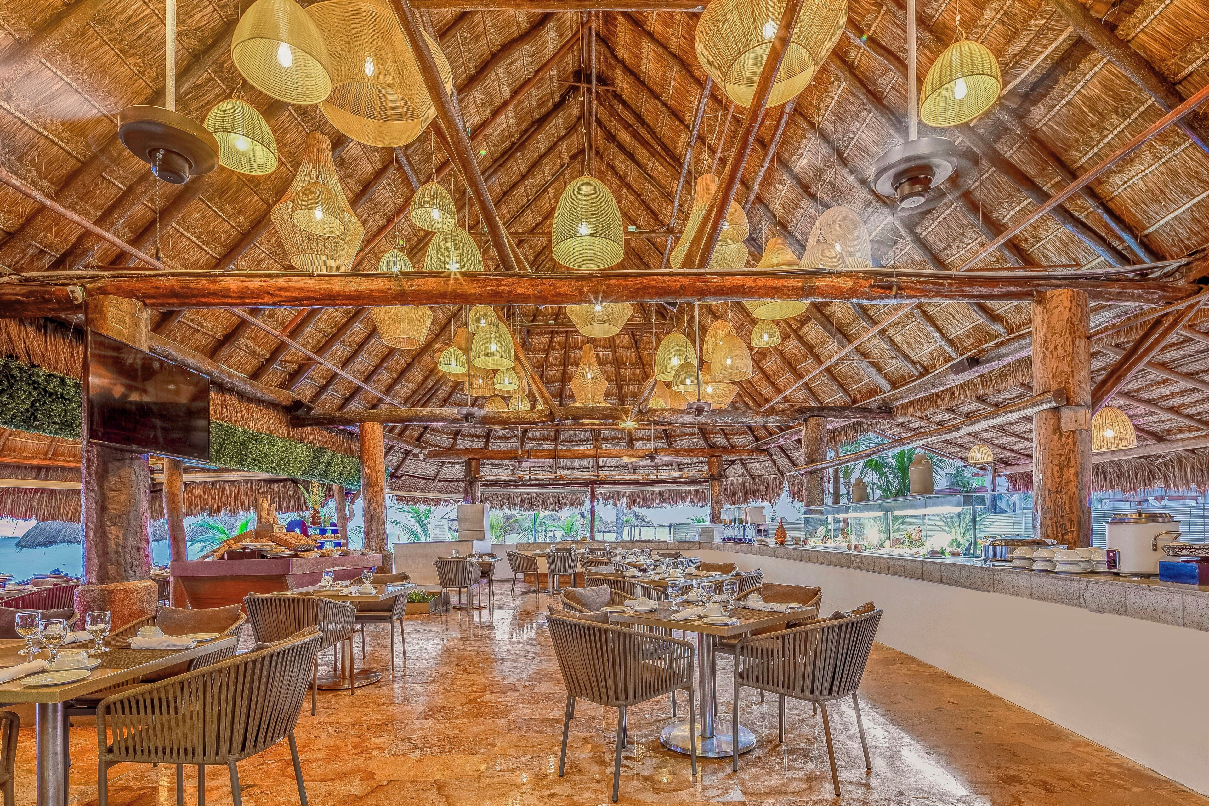 Un restaurant doté d’un toit de chaume, de plusieurs luminaires suspendus et offrant une vue sur la mer.