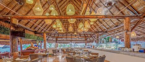 Un restaurant doté d’un toit de chaume, de plusieurs luminaires suspendus et offrant une vue sur la mer.