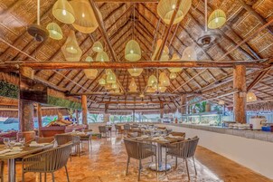 Un restaurante con techo de paja, múltiples lámparas colgantes y vistas al mar.