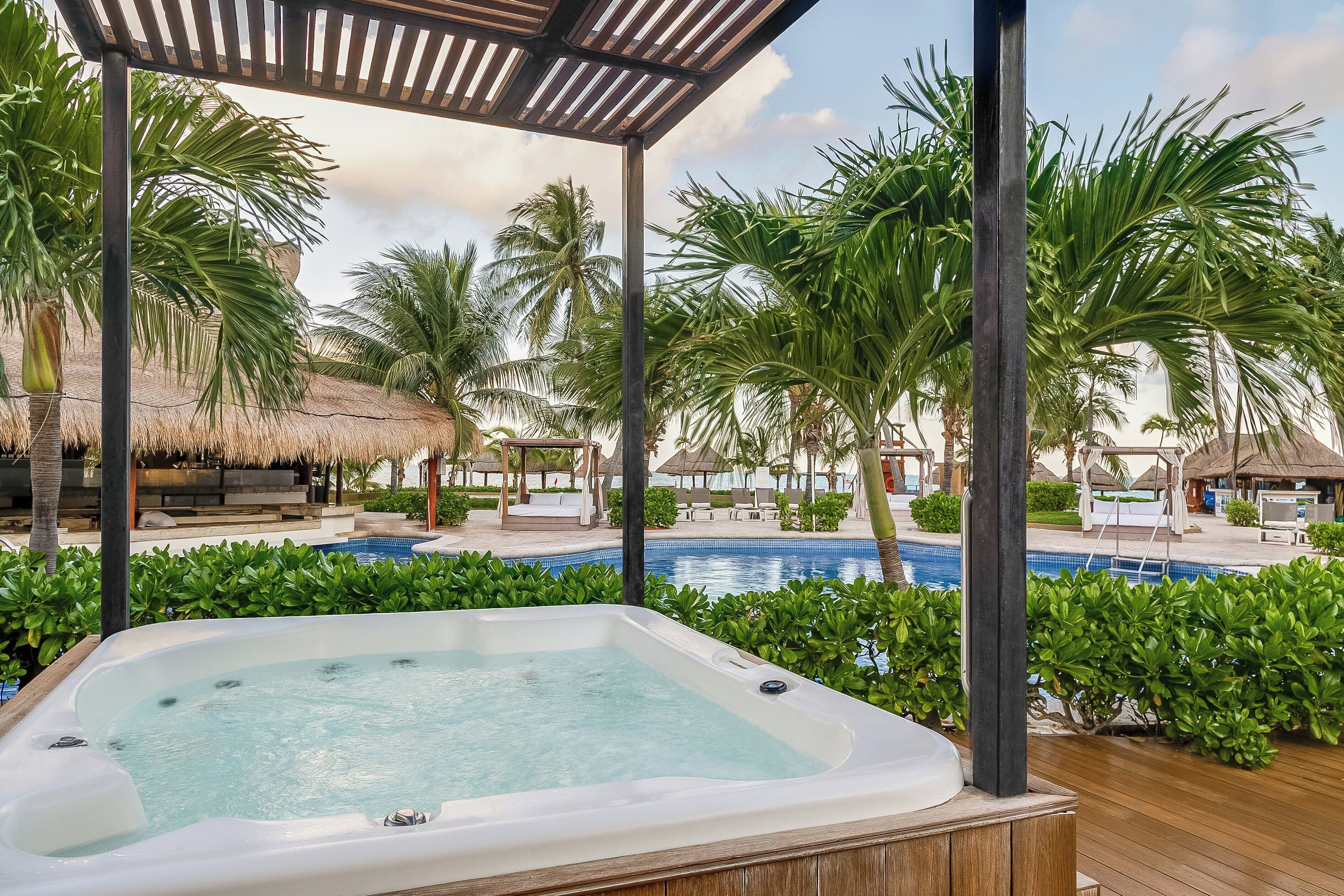A hot tub, a pool, and thatched-roof structures in a resort setting.