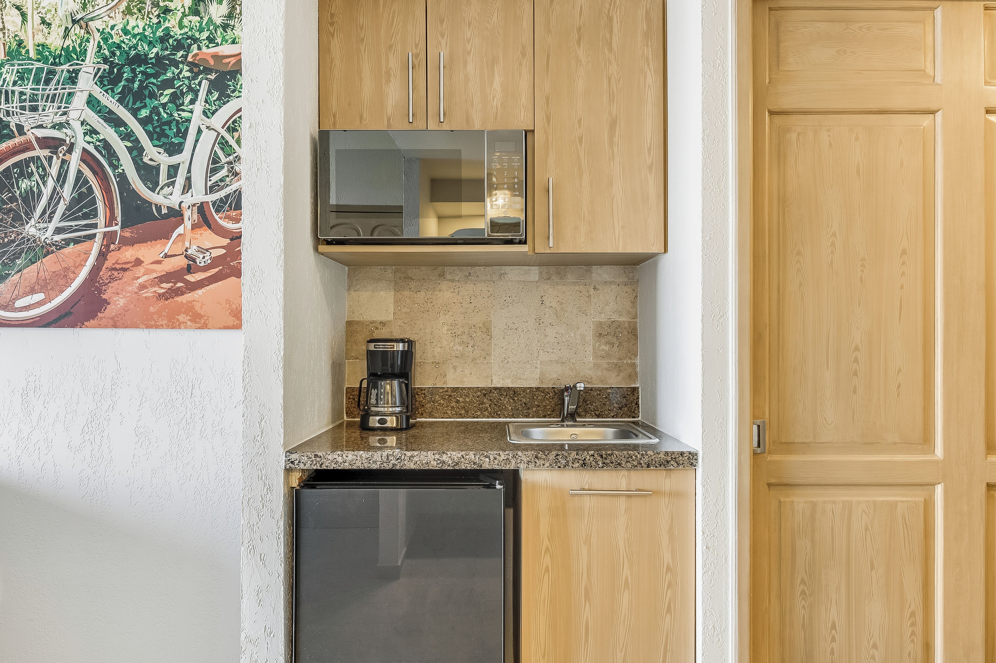 A compact kitchen with wooden cabinets, a microwave, a coffee maker, and a sink.