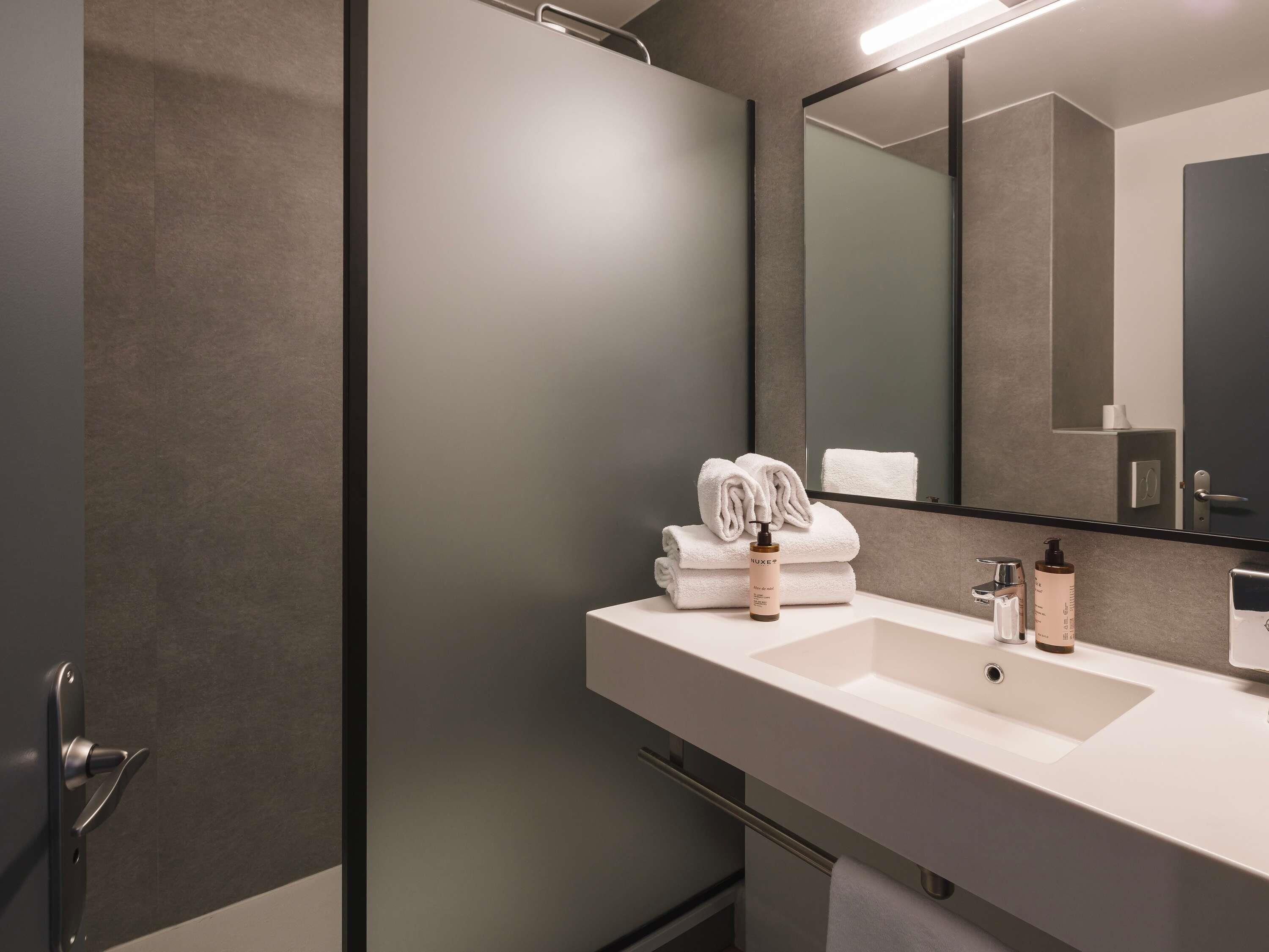 A modern bathroom with a large mirror, a white sink, and neatly folded towels.