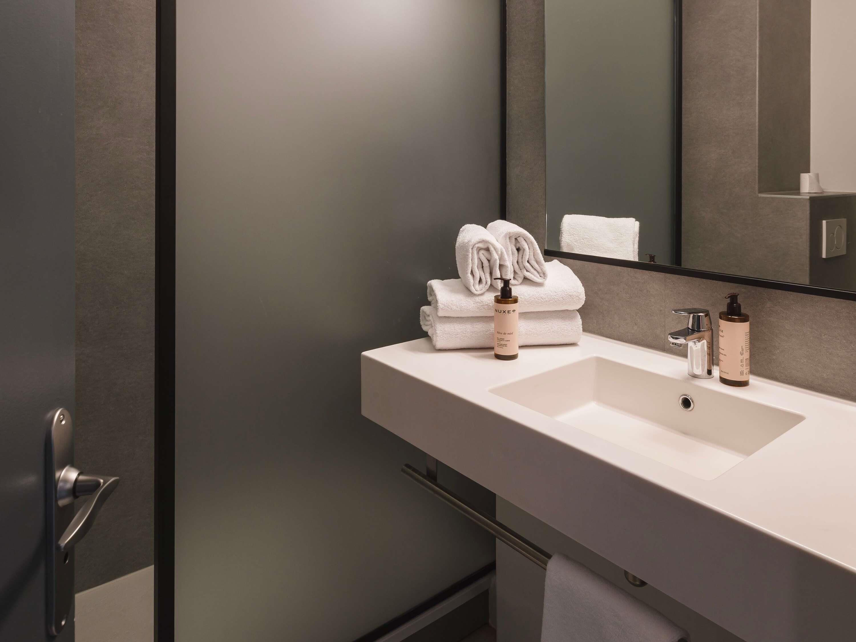 Un baño moderno con un lavamanos blanco, un espejo y toallas dobladas con cuidado.
