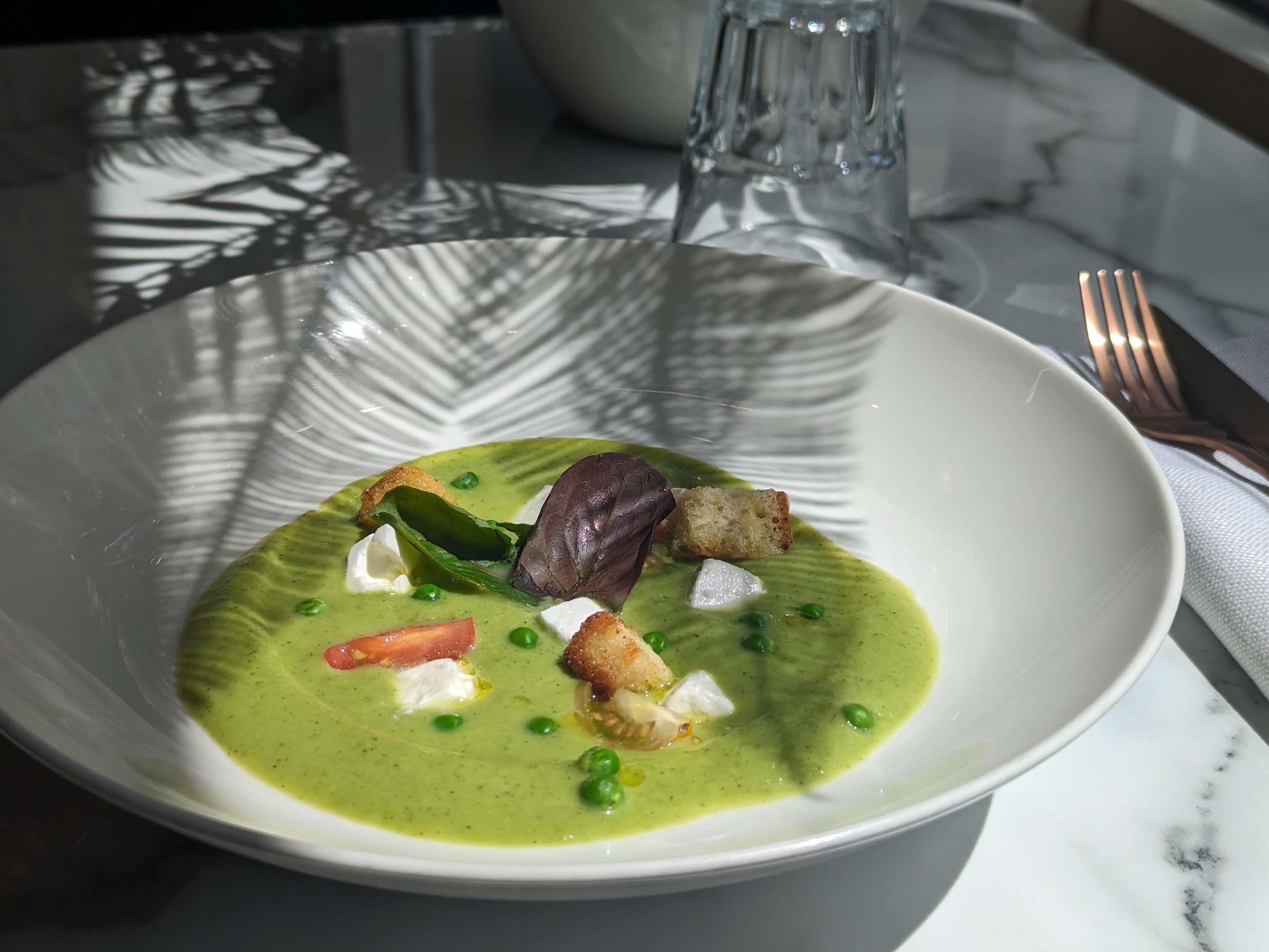 A white plate with a green soup, croutons, and a leafy garnish on a marble table.