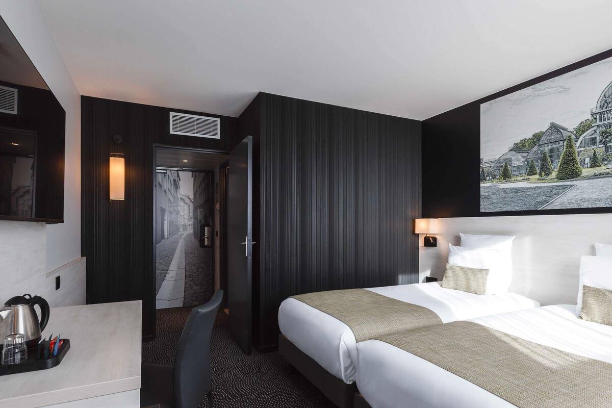A hotel room with a bed, a desk, a chair, a coffee maker, and a painting on the wall.