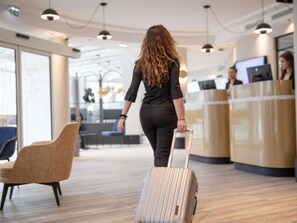 Eine Frau mit Koffer in einer modernen Hotelhalle mit Sitzgelegenheiten und einer Rezeption.