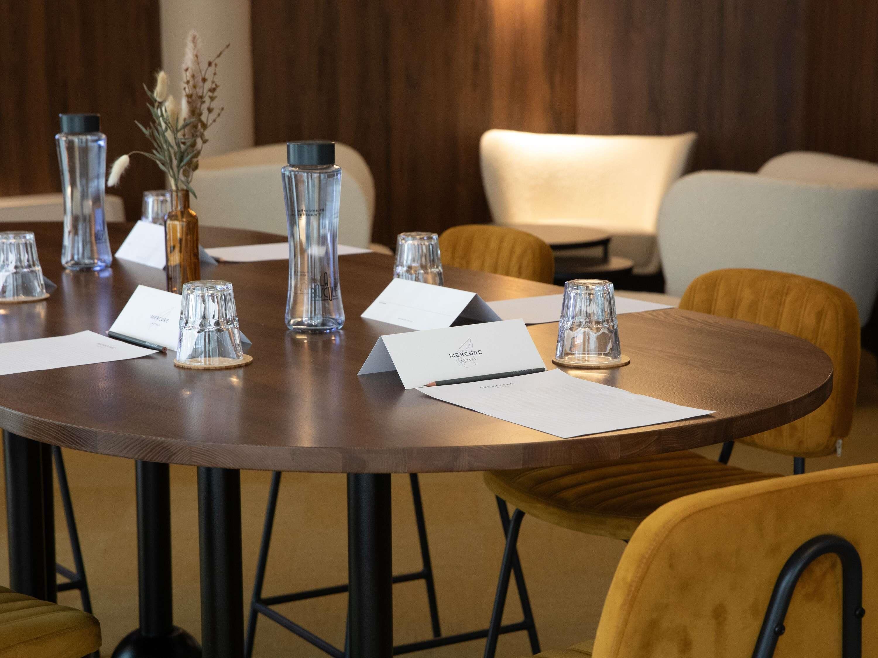 A conference table with name cards, glassware, and a vase with dried flowers.