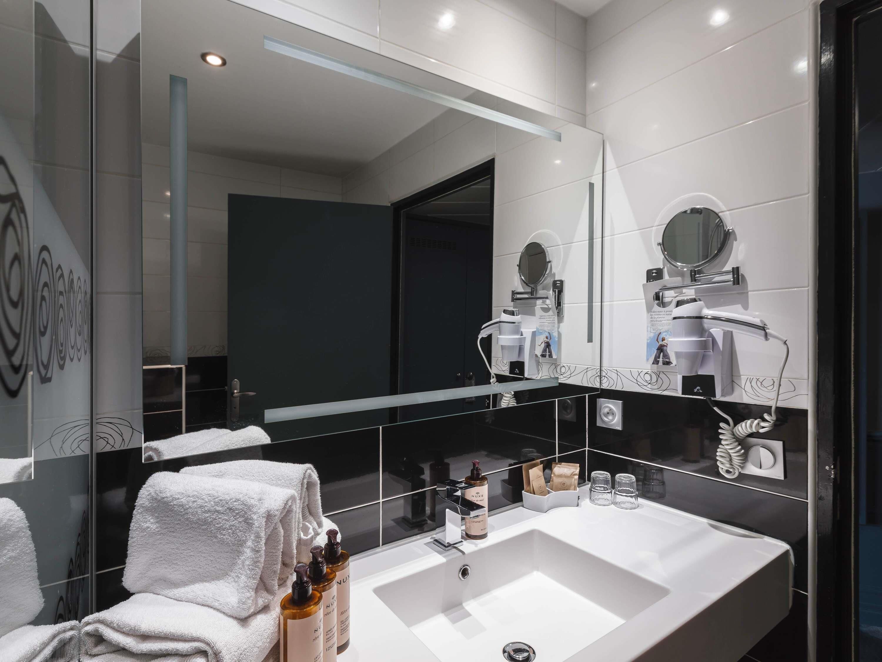 A modern bathroom with a large mirror, a sink, and a towel rack.