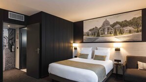 A hotel room with a large bed, a desk with a chair, a wall-mounted TV, and a door leading to a corridor. - Mercure Lyon Centre Charpennes Parc de la Tete d'Or (Villeurbanne)