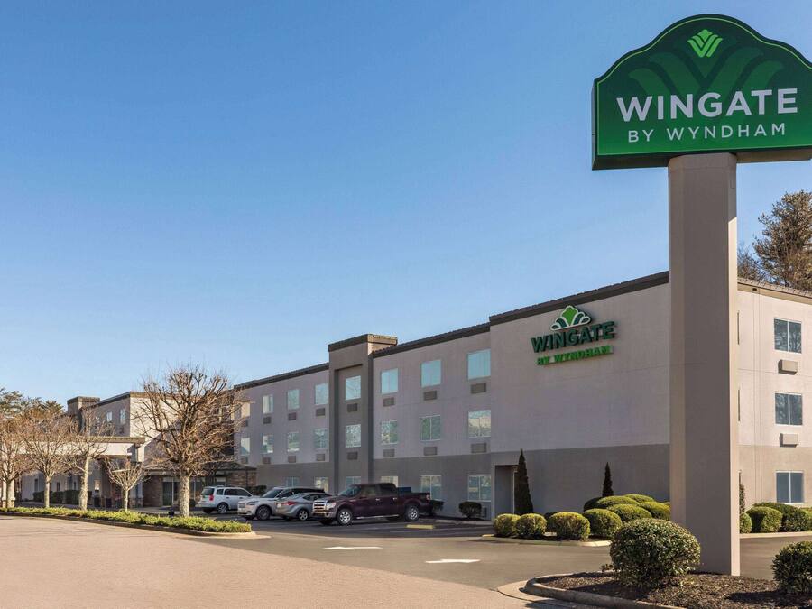Un hotel Wingate by Wyndham con una fachada moderna, varios pisos y un estacionamiento con varios autos.