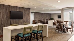 A modern conference room with a long table, several chairs, a flat-screen TV mounted on the wall, and a large window providing natural light.
