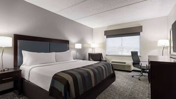 A hotel room with a large bed, two bedside tables with lamps, a desk with a chair, a window with a view, and a wall-mounted TV.