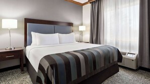 A hotel room with a large bed, two bedside tables, a window with curtains, and an air conditioning unit.